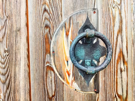Forged metal handle on a wooden door. Background, texture. Close-up of a handcrafted metal door handle on weathered wood