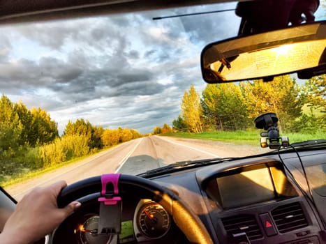 Car salon, windshield, hand of woman on steering wheel and landscape. View from seat of female driver on nature and Road, trees, blue sky at sunny day