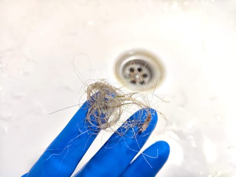 Removing Hair Clog From a Bathroom Sink Drain. Gloved hand extracting hair from sink