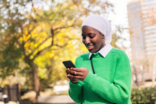 muslim black woman smiling happy using her mobile phone, concept of technology and modern lifestyle, copy space for text