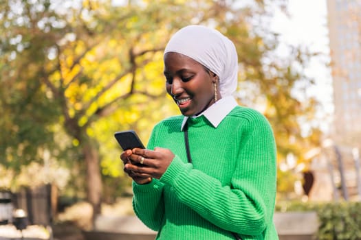 muslim black woman smiling happy using her mobile phone, concept of technology and modern lifestyle
