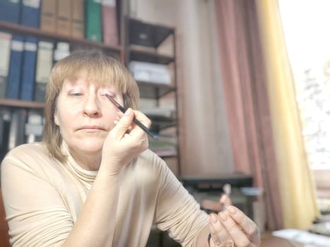 Portrait of a middle-aged woman doing eye makeup. Selfie portrait of lady who is businesswoman, accountant, manager, freelancer doing morning makeup at office on working place