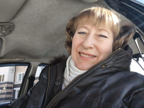 Middle aged woman in a car taking a selfie while enjoying a drive. Female mature driver posing inside car. Funny happy tourist girl in alone travel