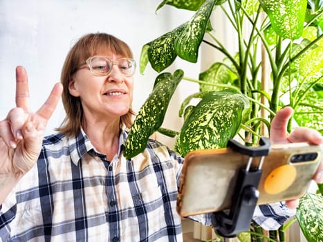 Smiling woman in glasses using a smartphone on a tripod for a video chat. A middle-aged woman posing and taking a selfie