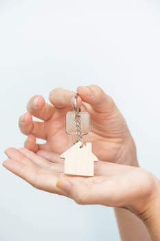 Close-up of beautiful hands of a woman with the new home keys. Keychain in the shape of a wooden house on white background. High quality photo