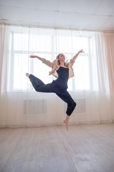 Caucasian woman dances contemporary in ballet class. Dancer in a jump. Vertical photo