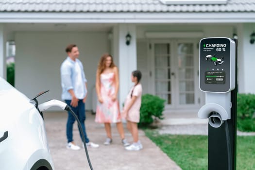 Focused electric vehicle recharging battery from home charging station for EV car powered by alternative and sustainable energy for modern environmental family on blurred background. Synchronos