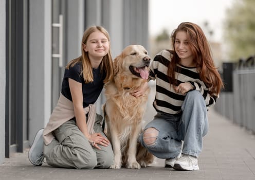 Two Girls With Golden Retriever Sitting And Playing Outside In Spring
