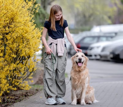 Girl Strolls Down Street With Golden Retriever In Spring