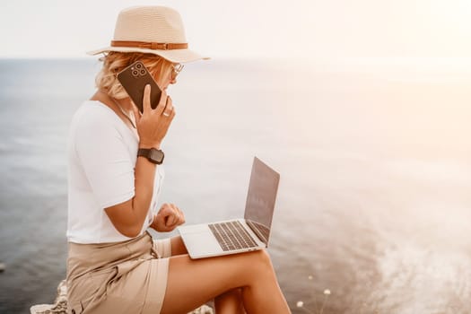 Digital nomad, Business woman working on laptop by the sea. Pretty lady typing on computer by the sea at sunset, makes a business transaction online from a distance. Freelance remote work on vacation