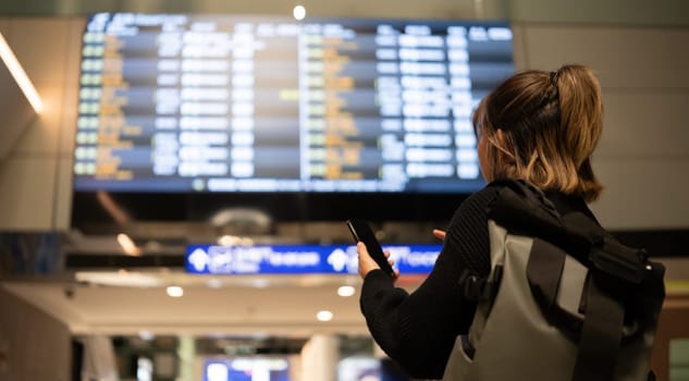 Young Asian woman in international airport looking at flight information board, checking her flight.