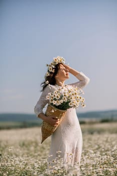 Happy woman in a field of daisies with a wreath of wildflowers on her head. woman in a white dress in a field of white flowers. Charming woman with a bouquet of daisies, tender summer photo.