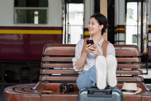 Young woman with backpack checking social media on phone waiting for train at train station to travel.