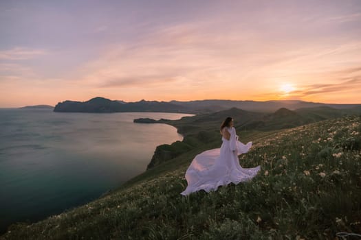 A woman in a white dress is walking on a grassy hill overlooking a body of water. The scene is serene and peaceful, with the sun setting in the background. The woman is enjoying the beautiful view