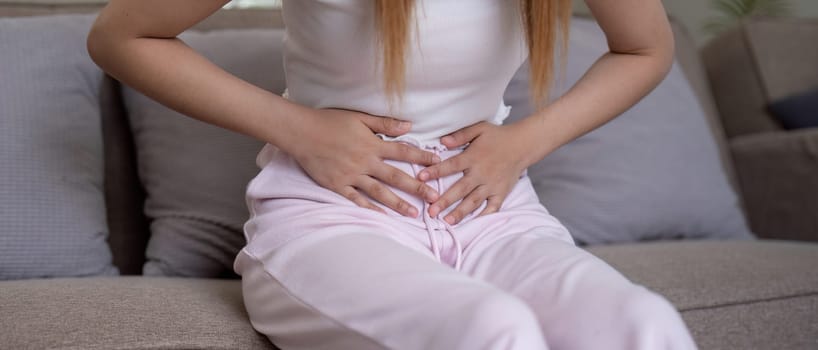 Young woman suffering from stomach ache on sofa at home.