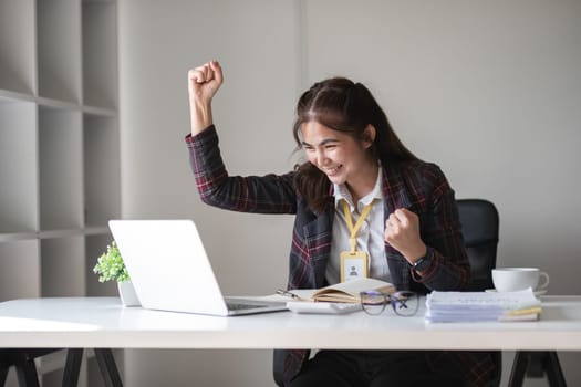 Asian female office worker expresses happiness at success at work View the announcement results on the laptop in the office..