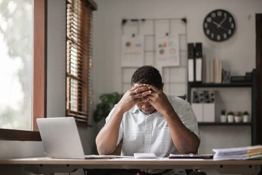 African American businessman feeling stressed while working using laptop Take notes on documents in the office and prepare work reports..