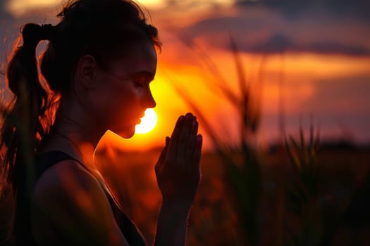 A woman is praying in a field with the sun in the background