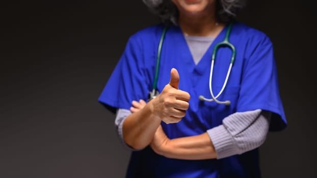 Senior doctor with stethoscope showing thumbs up over black background . Medical and health care concept.