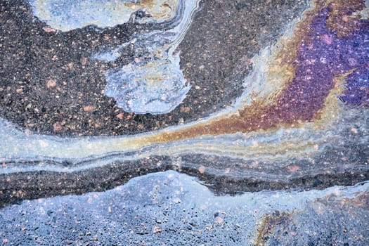 An overhead shot of the mesmerizing patterns created by leaking gasoline on wet ground