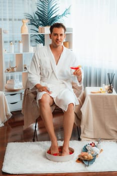 Beauty or body treatment spa salon vacation lifestyle concept with man wearing bathrobe relaxing with drinks in luxurious hotel spa or resort room. Vacation and leisure relaxation. Quiescent