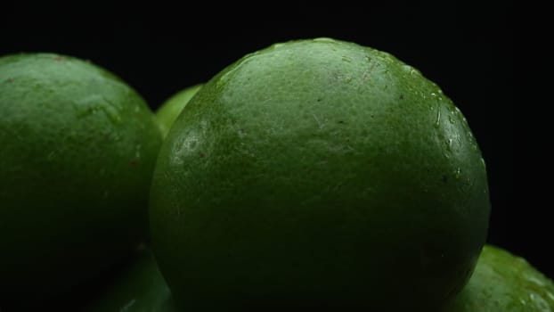 Slices of lime are meticulously arranged in a pile, set against a black background. Each lime slice is captured in stunning detail, its vibrant green hue and enticing texture. Close up. Comestible.