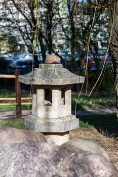 A stone lantern sits beside a tree in a park, adding a touch of art to the natural landscape. The lantern contrasts beautifully with the green grass and wood trunk of the tree