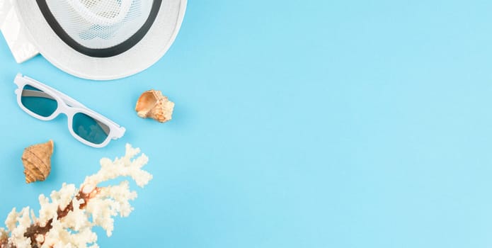 Beach hat with sunglasses on blue isolated background with copy space. Flat lay. Summer vacation concept. Seashells top view.