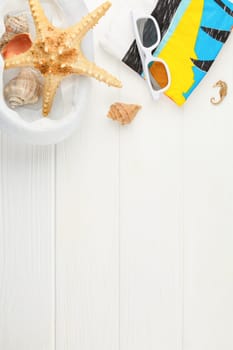 Beach hat with towel and sunglasses on white wooden background. Banner with copy space. Summer vacation concept. Flat lay. Starfish and seashells. Vertical photo.