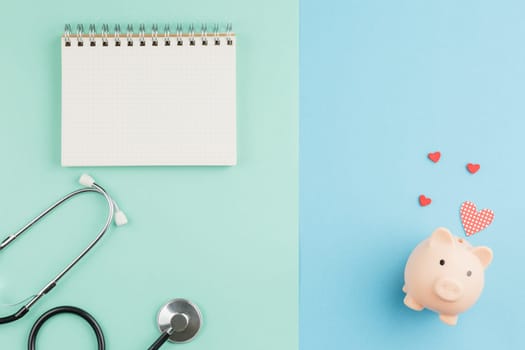 Open spiral notebook. Charity for medicine. Pig piggy bank with red hearts and a stethoscope on a two color background. Donations and volunteering concept. Top view, flat lay.