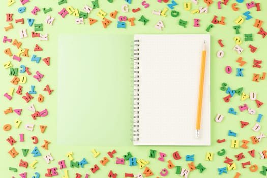 Colored letters of the alphabet on a green background. Top view. Open school notebook with a pencil. Back to school concept.