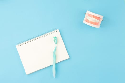 Dental concept. Oral hygiene. Spiral notepad with tooth brush on blue background. Model of the jaw on the dentist table top view.