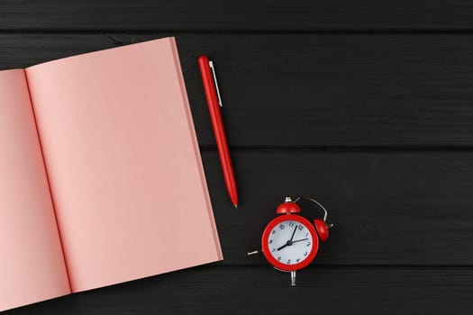 Pink open notebook with alarm clock and a pen on red isolated background top view.