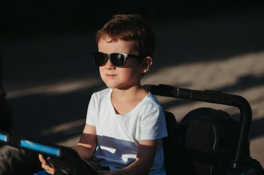portrait of a child boy in sunglasses in a toy mini car in the park in summer