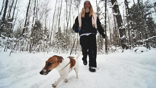 A girl and her Jack Russell Terrier dog are running through the woods