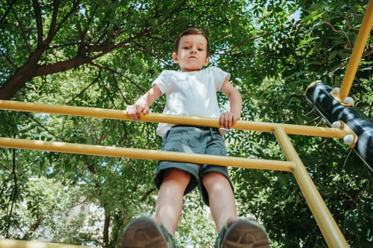 child boy playing and climbing on horizontal bars on the playground in summer