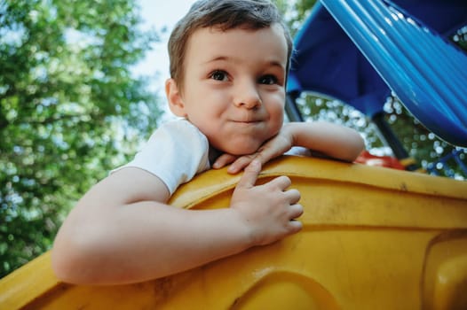 happy child kindergarten boy playing on a slide on the playground in summer