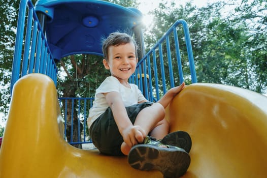 happy preschooler boy playing on a slide on the playground in summer