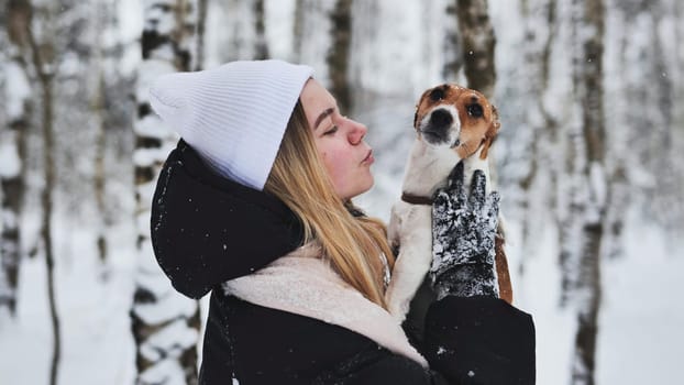 A girl cuddles a Jack Russell Terrier dog in the woods in winter