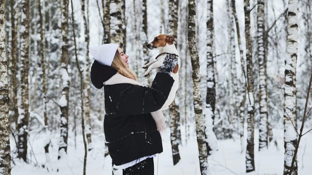 A girl tosses up her Jack Russell Terrier dog in the woods in winter