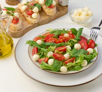 Salad with mozzarella, cherry tomatoes and green lettuce in a white round plate on the table, close up