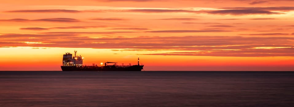 Silhouette of cargo Ship at horizon against of Amazing red sunrise