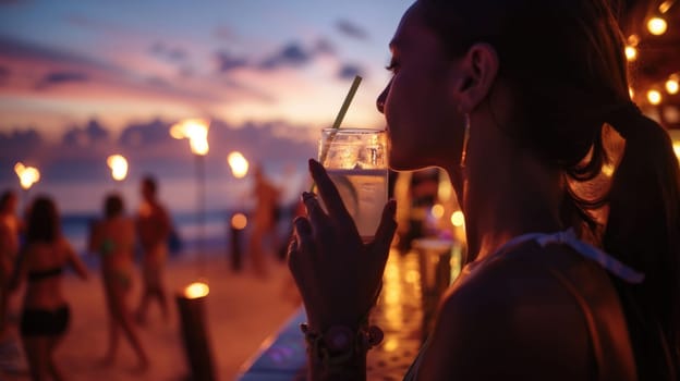 Under the midnight sky, a woman is enjoying a refreshing drink of water through a straw on the beach. The sound of music adds to the fun atmosphere during this latenight beach event AIG50