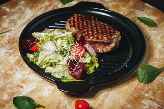 Grilled Steak Served WA succulent grilled steak accompanied by a colorful salad on a black plate, garnished with herbs.ith Fresh Garden Salad on a Black Plate. High quality photo