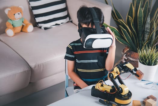 Asian kid boy using VR glasses on robotic arm in workshop, Child learning programer control robot arm with sensors to pick up wood block, Technology education, Virtual Reality Simulator, industry 4.0