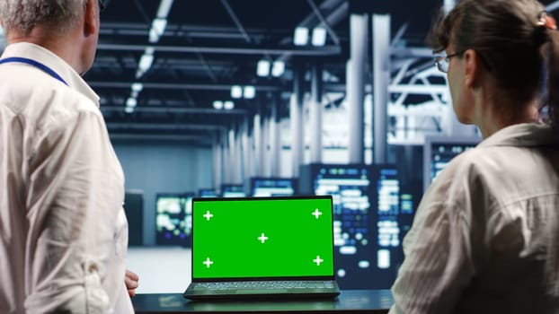 Trained computer scientists looking around high tech data center, using mockup laptop to crosscheck disaster recovery plan and assess server systems in need of replacement, preventing collapse