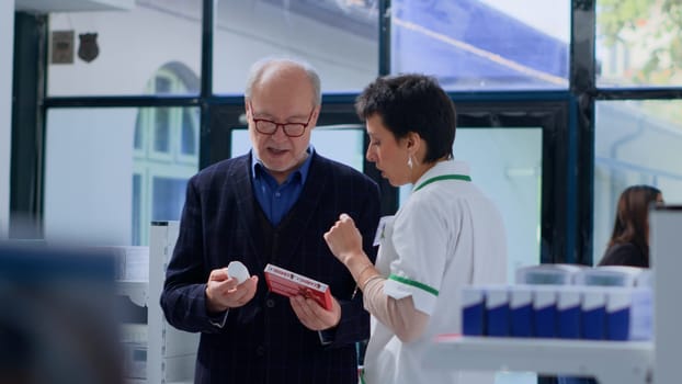 Proficient pharmacy heart specialist helping elderly man with medical suggestions. Senior client in dispensary wishing to purchase cardiologist prescribed medicaments, asking expert for guidance