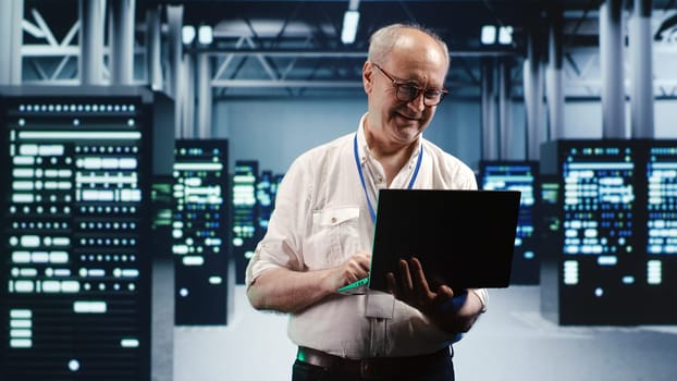 Capable serviceman expertly managing data while navigating in industrial server room. Proficient repairman in high tech facility ensuring optimal cybersecurity protection, optimizing systems