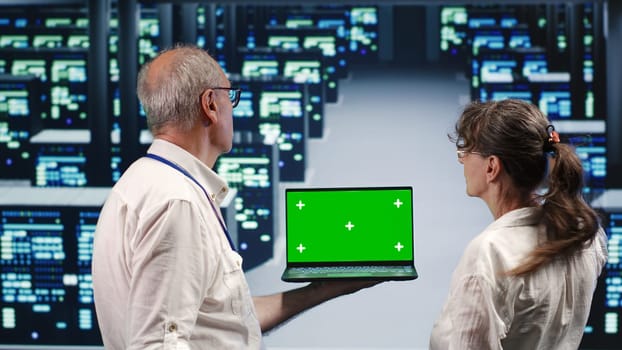 Experienced professionals looking around high tech data center, using mockup laptop to crosscheck disaster recovery plan and assess server infrastructure in need of replacement, preventing issues