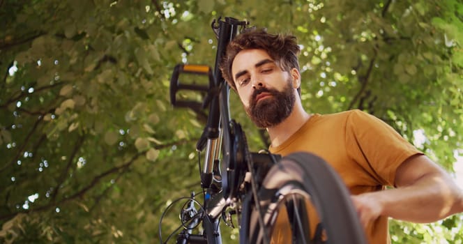 Athletic caucasian man accurately adjusting and securing bicycle pedal and crank arm. Fit male cyclist inspecting damaged bike in yard ready to repair on professional repair-stand. Dolly zoom-out.